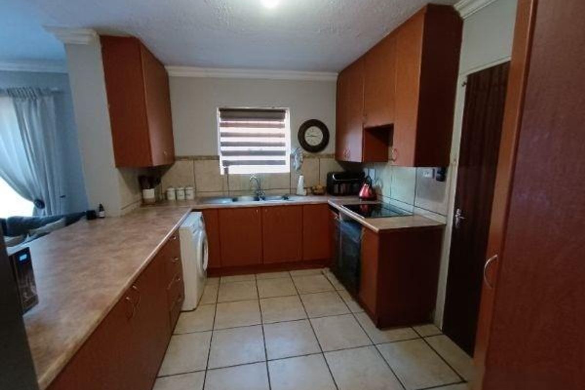 A functional kitchen featuring wooden cabinetry, laminate countertops, a double basin sink, and built-in cooking appliances with tiled flooring throughout.