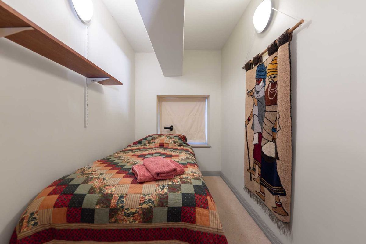 A compact bedroom featuring wall-mounted shelving, recessed window, and wall-mounted lighting fixtures.