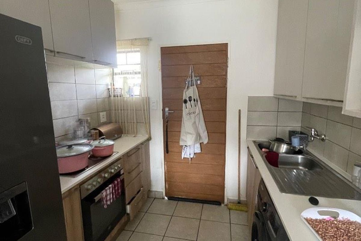 Functional galley-style kitchen featuring built-in cabinetry, tiled backsplash, integrated oven and hob, and tiled flooring with direct access to an exterior door.