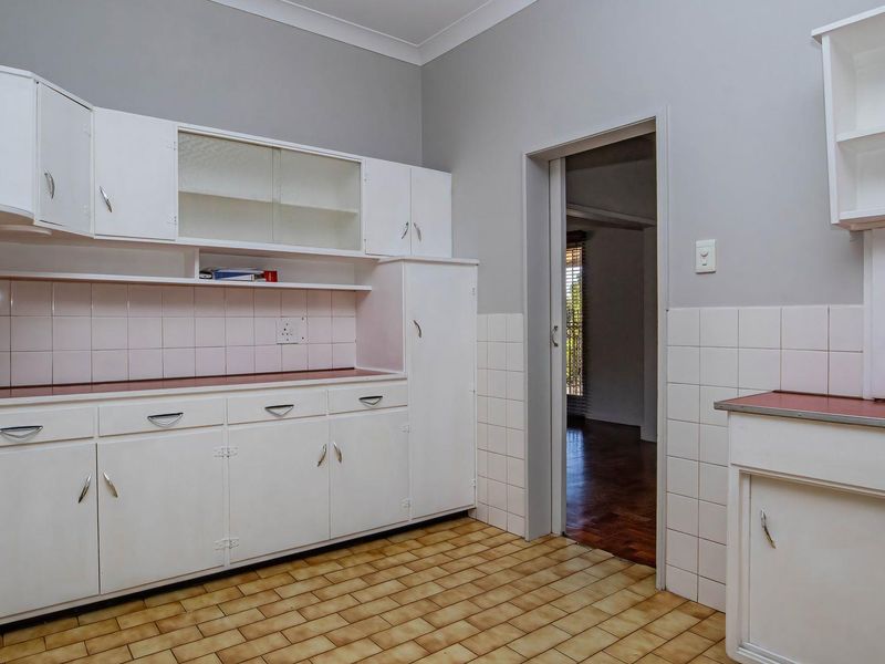 A functional kitchen space featuring white built-in cabinetry, tiled splashbacks, and durable tiled flooring, offering a blank canvas for modern renovation.