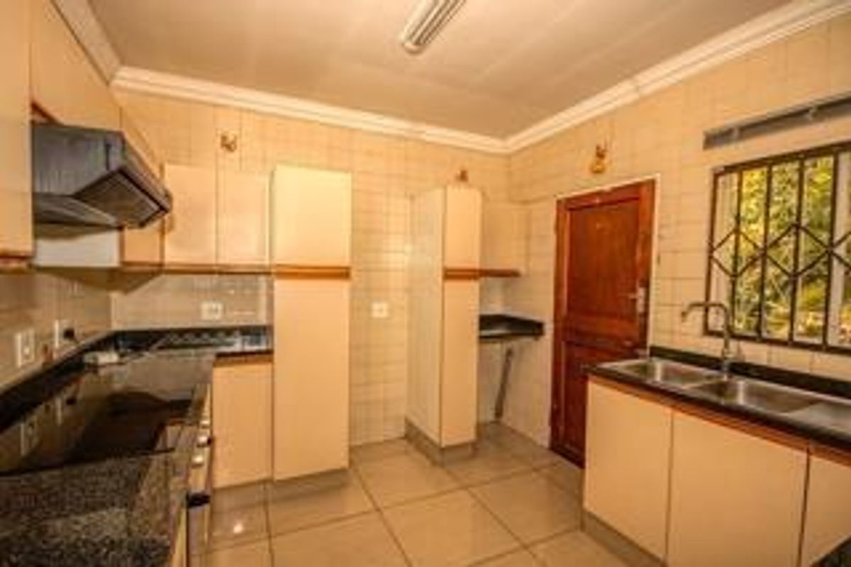 A functional kitchen featuring granite countertops, ample built-in cabinetry, a double basin sink, and tiled finishes throughout.