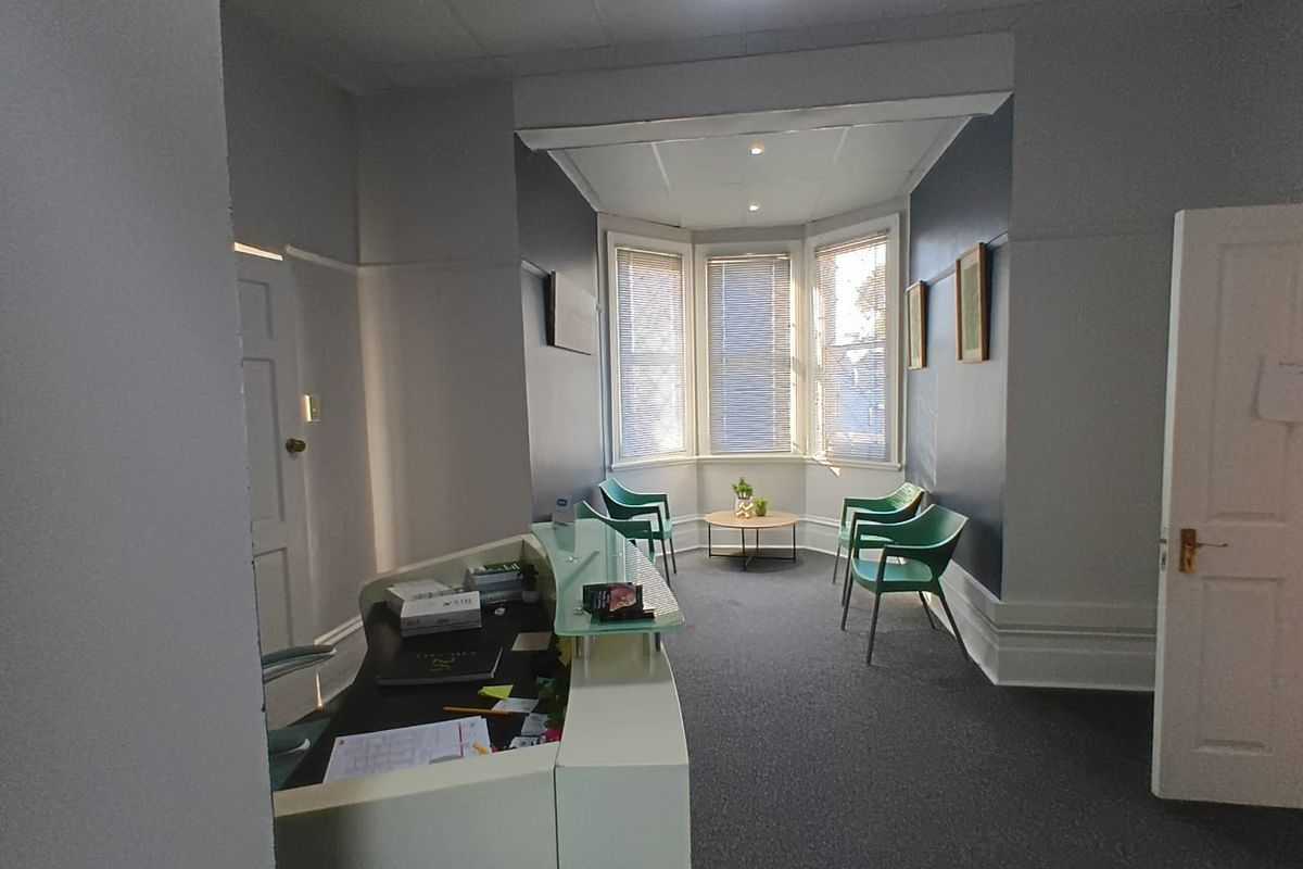 A professional office reception area featuring a built-in reception desk, a bright bay window with venetian blinds, and neutral carpeting.