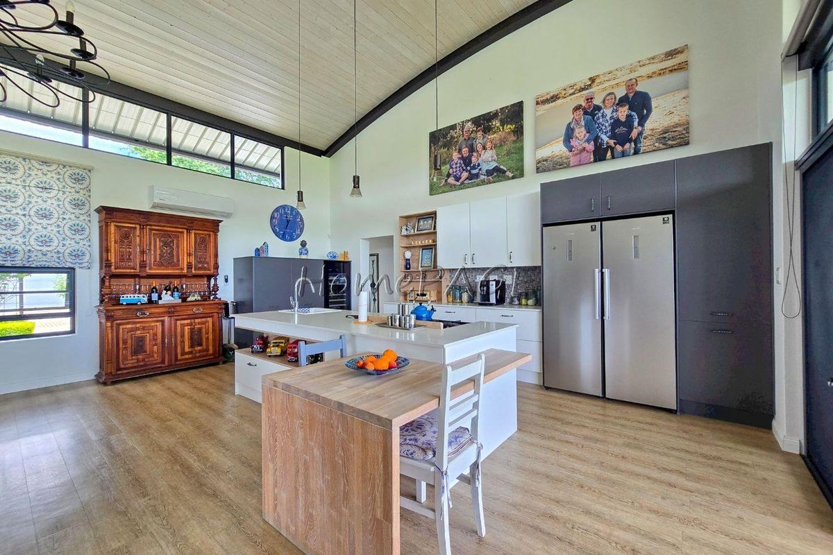 Modern open-plan kitchen featuring a central island with breakfast bar, sleek cabinetry, integrated appliances, and high vaulted ceilings with clerestory windows.