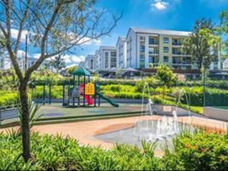 A well-maintained communal outdoor area featuring a children's playground, water fountain feature, and landscaped gardens within a townhouse complex.