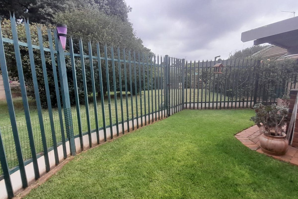 A private rear garden featuring a well-maintained lawn, brick-paved patio area, and secure metal perimeter fencing.
