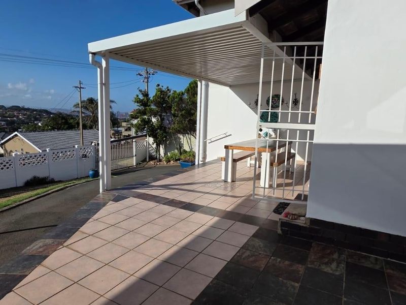A covered outdoor patio area featuring tiled flooring, a louvred roof structure, and a security gate, offering a functional space for outdoor living.