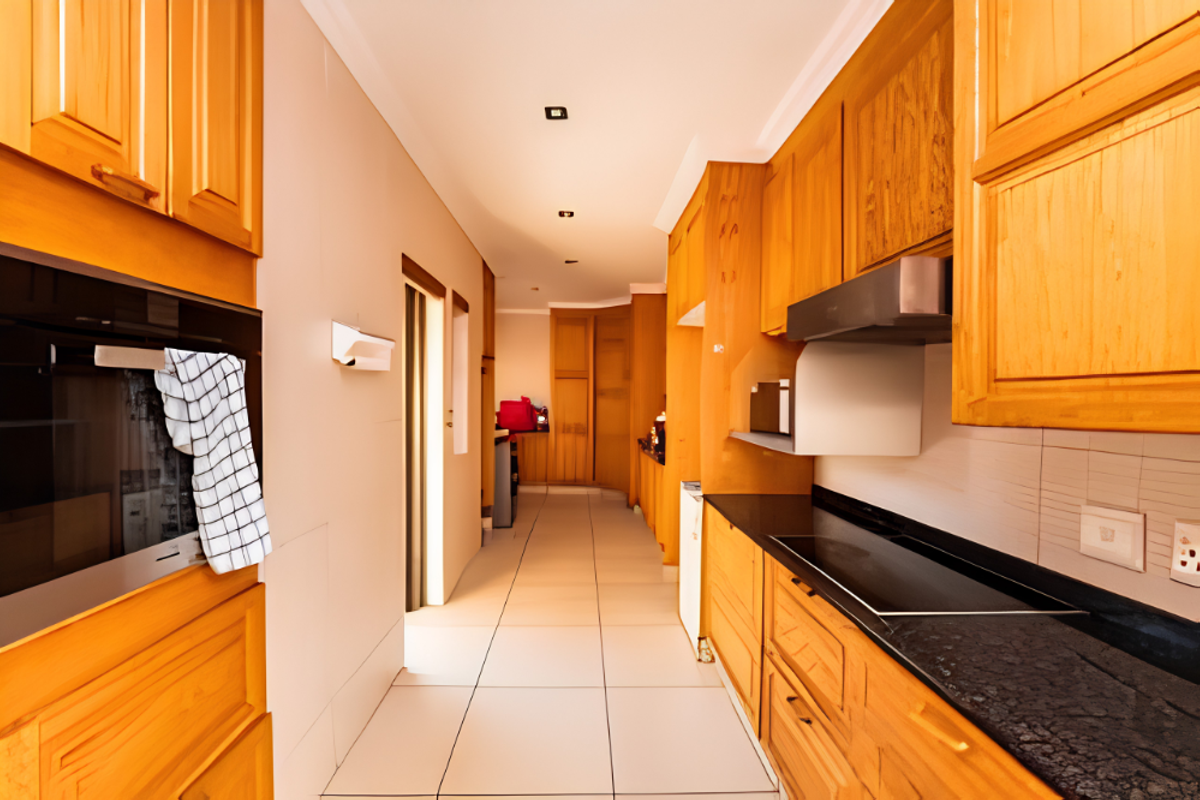 A galley-style kitchen featuring warm-toned wooden cabinetry, black granite countertops, integrated oven, and a sleek electric hob with an extractor fan.