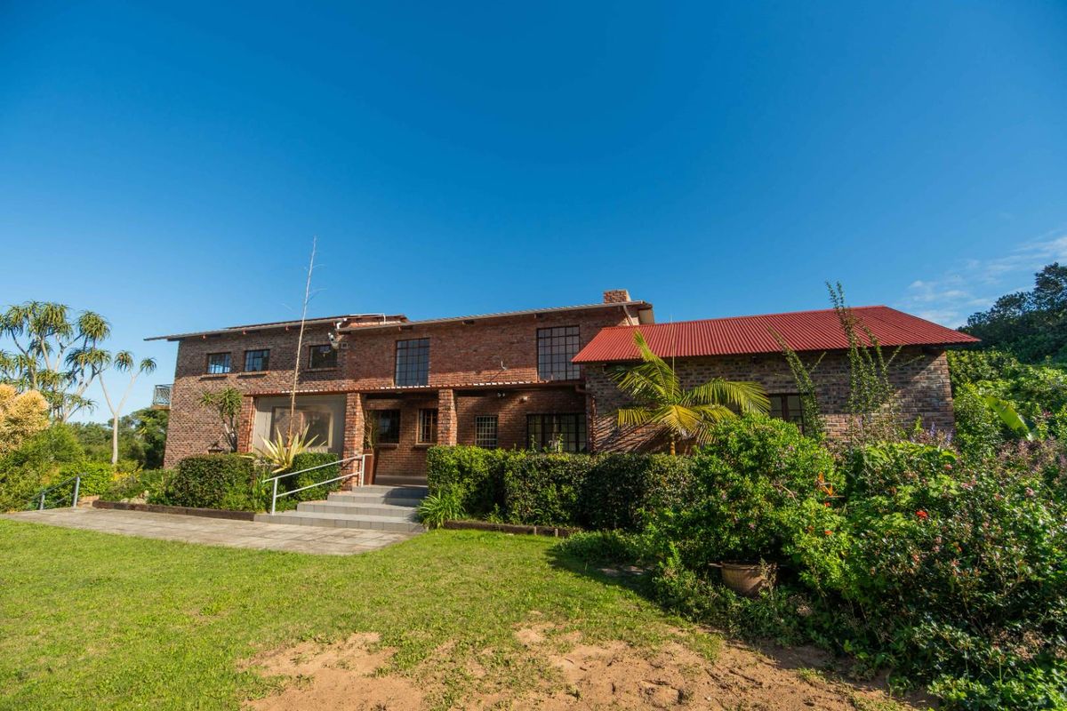 A rear view of a two-story exposed brick house featuring a red corrugated metal roof, concrete entrance steps, and a surrounding landscaped garden.