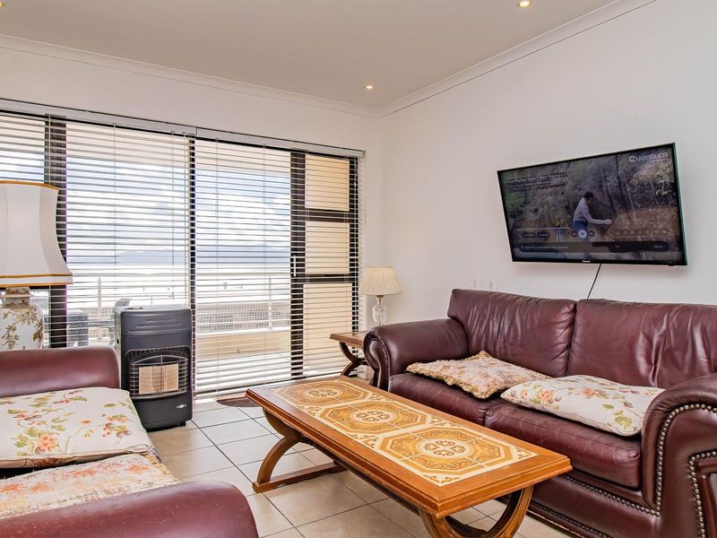A bright living room featuring tiled flooring, coved ceilings, and a large sliding glass door with venetian blinds leading to an outdoor area.