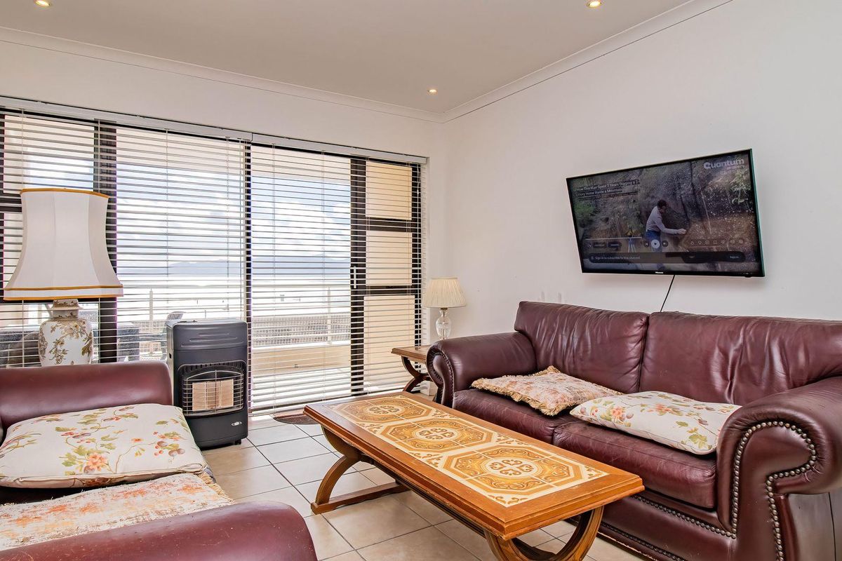 A bright living room featuring tiled flooring, coved ceilings, and a large sliding glass door with venetian blinds leading to an outdoor area.