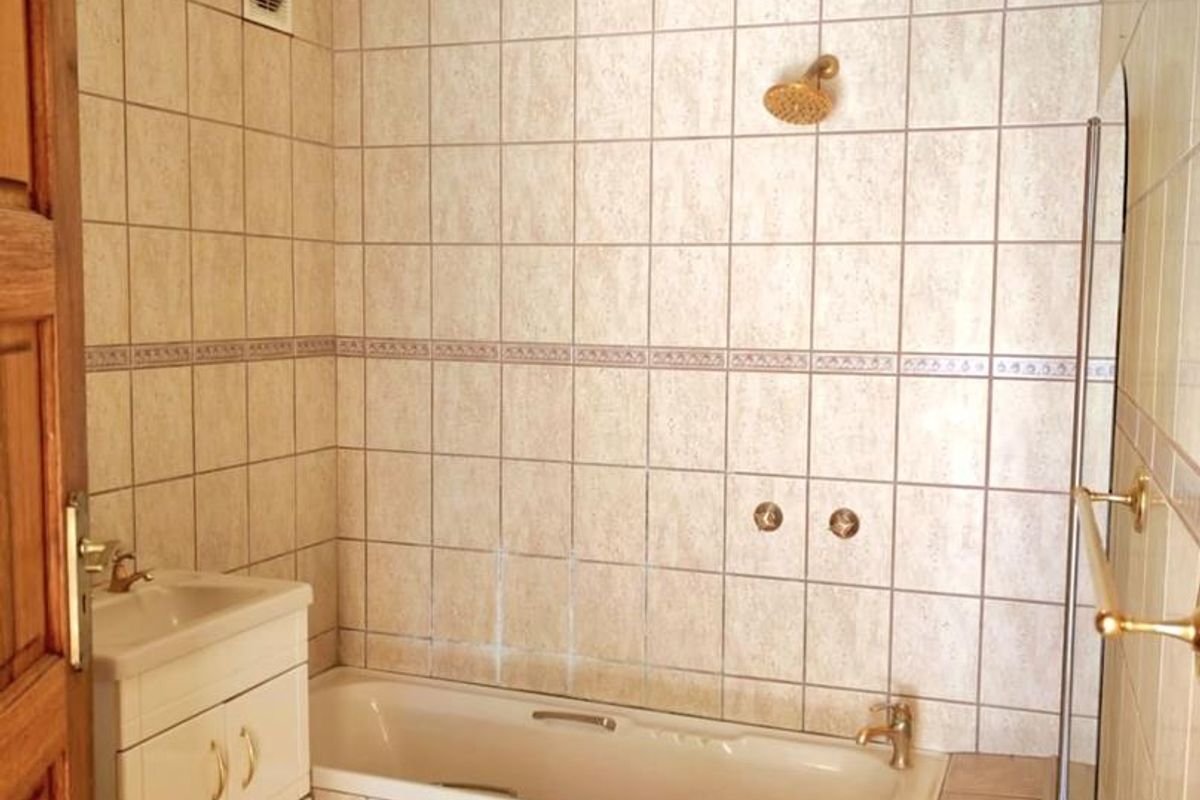 A functional bathroom featuring a built-in bathtub, shower head, vanity cabinet with basin, and full-height wall tiling.