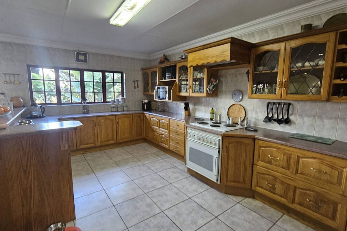 A spacious kitchen featuring traditional timber cabinetry, tiled flooring, a built-in oven and hob, and ample counter space with a breakfast bar.