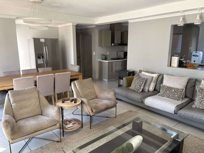 Spacious open-plan living and dining area featuring tiled floors, neutral walls, and a functional kitchen with modern cabinetry and built-in appliances.