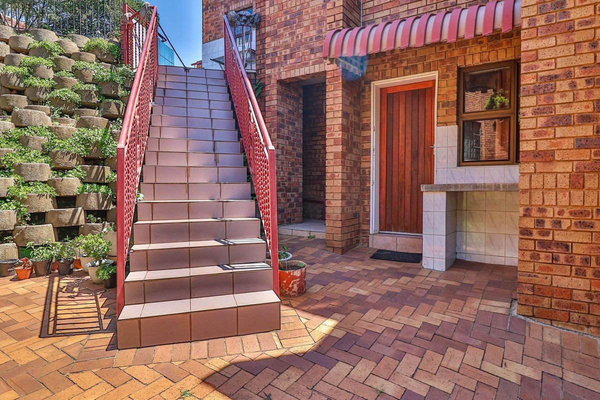 A rear exterior area featuring a brick-paved courtyard, a tiled staircase with metal railings, and a built-in outdoor counter against a brick facade.