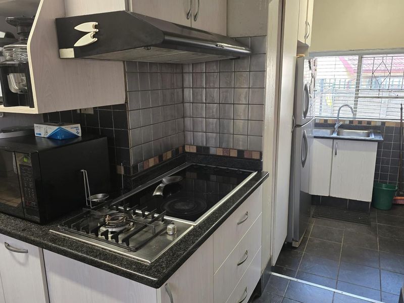 A functional kitchen featuring a dual gas and electric hob, granite countertops, tiled backsplash, and built-in cabinetry with a separate sink area.