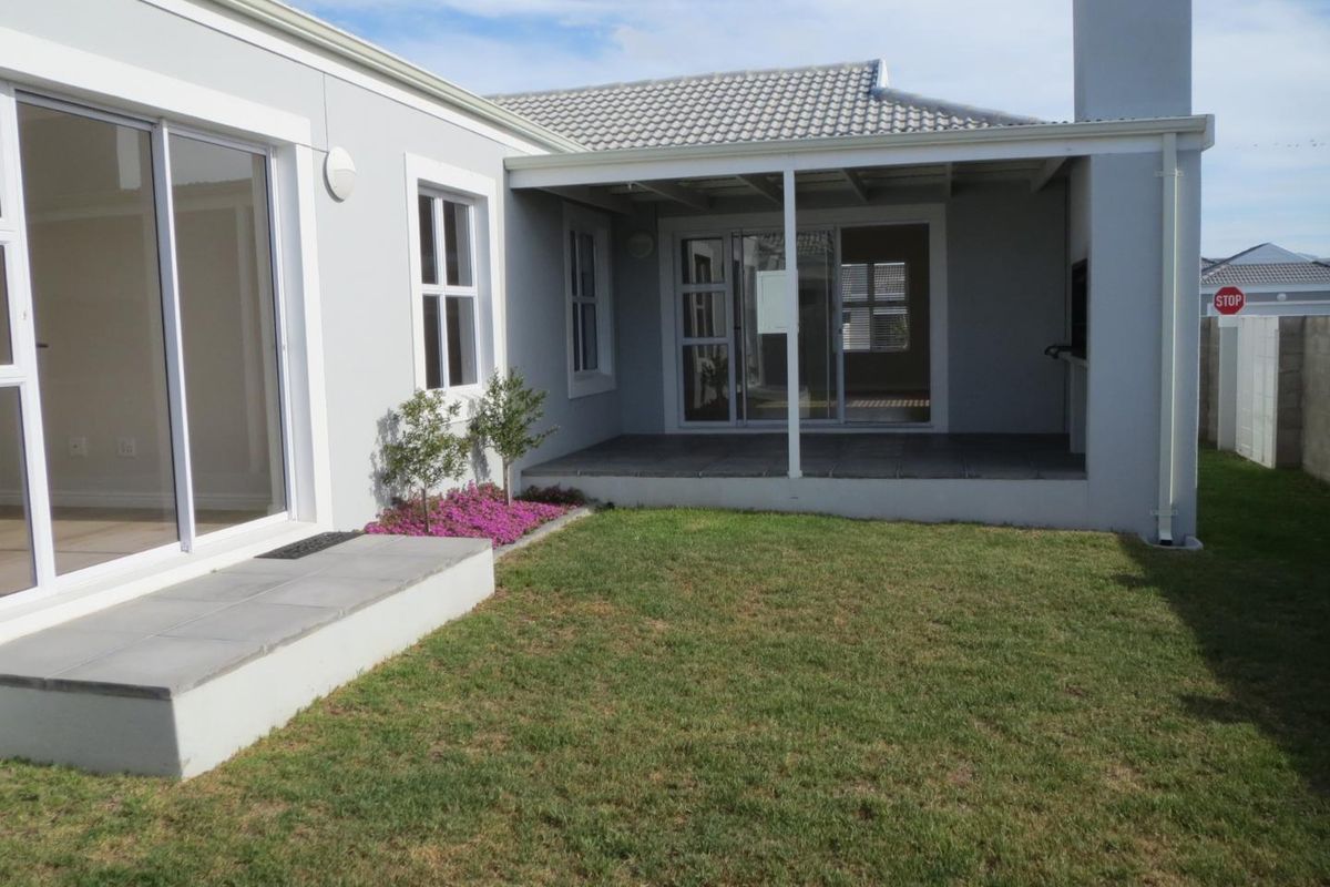 A well-maintained rear exterior featuring a covered patio with a built-in fireplace, sliding glass doors, and a neat lawn area.