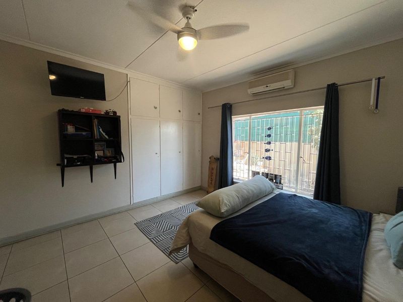 A functional bedroom featuring tiled flooring, built-in cupboards, a ceiling fan, and a wall-mounted air conditioning unit for climate control.