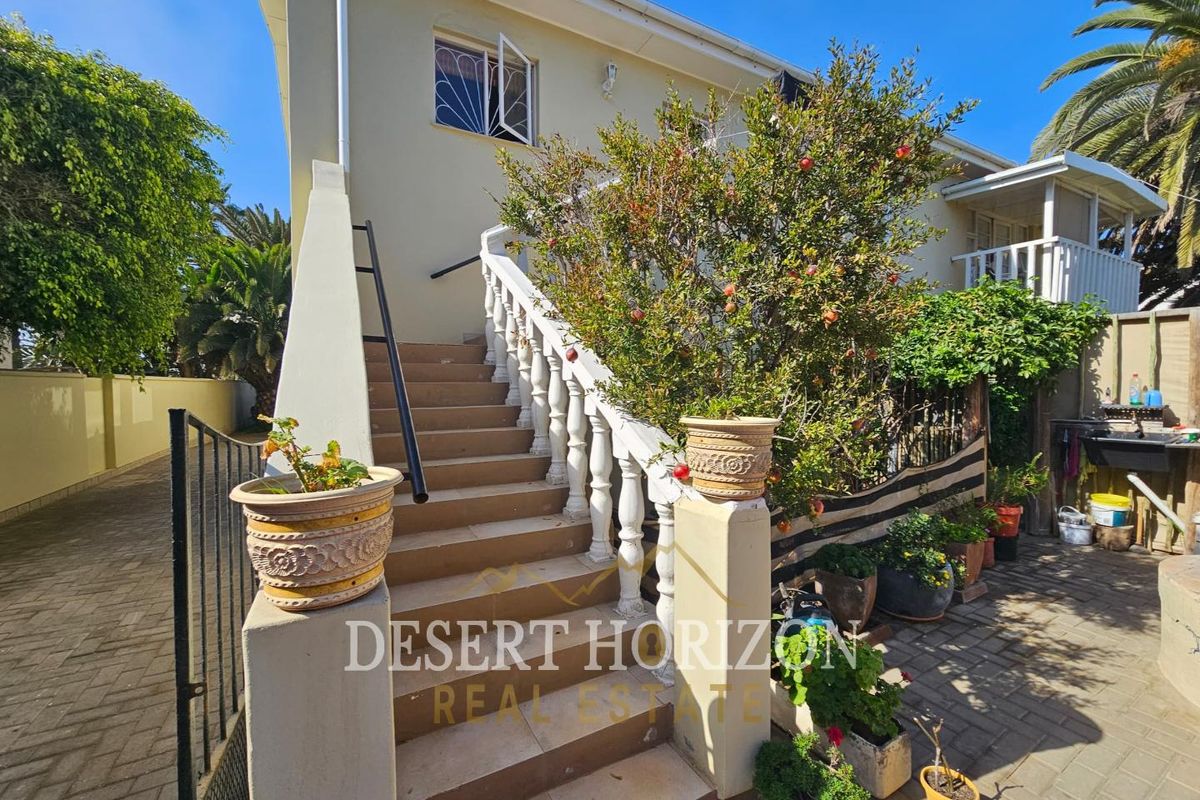 Exterior view of the property featuring a tiled staircase with decorative balustrades leading to an upper level entrance, set within a paved courtyard area.