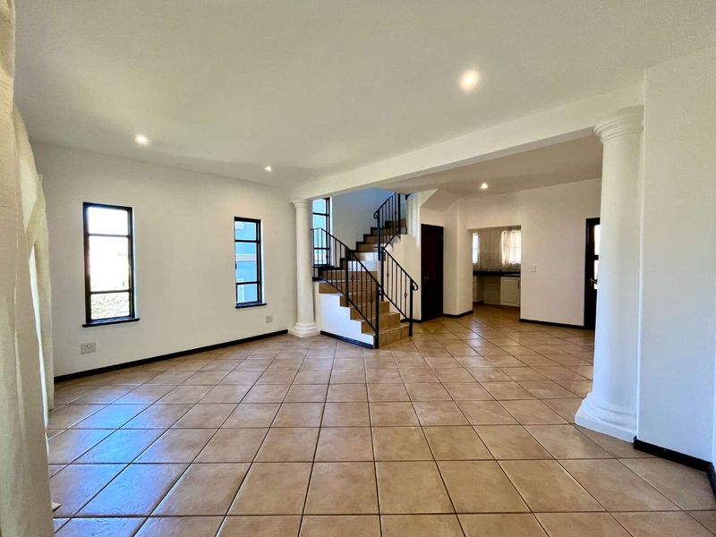 Spacious open-plan living area featuring tiled floors, decorative columns, and a central staircase with wrought iron balustrades, leading to a secondary kitchen area.