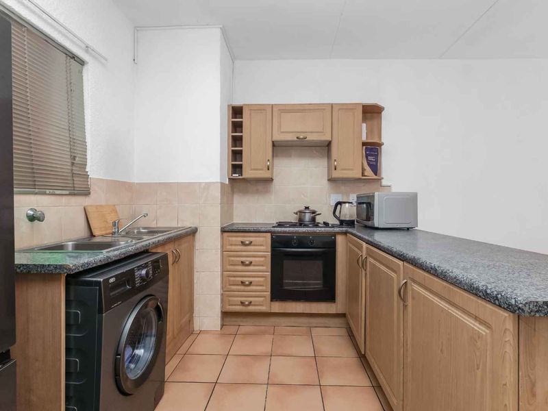 Functional kitchen featuring wood-finish cabinetry, granite-look laminate countertops, built-in oven and hob, tiled backsplash, and integrated laundry plumbing.
