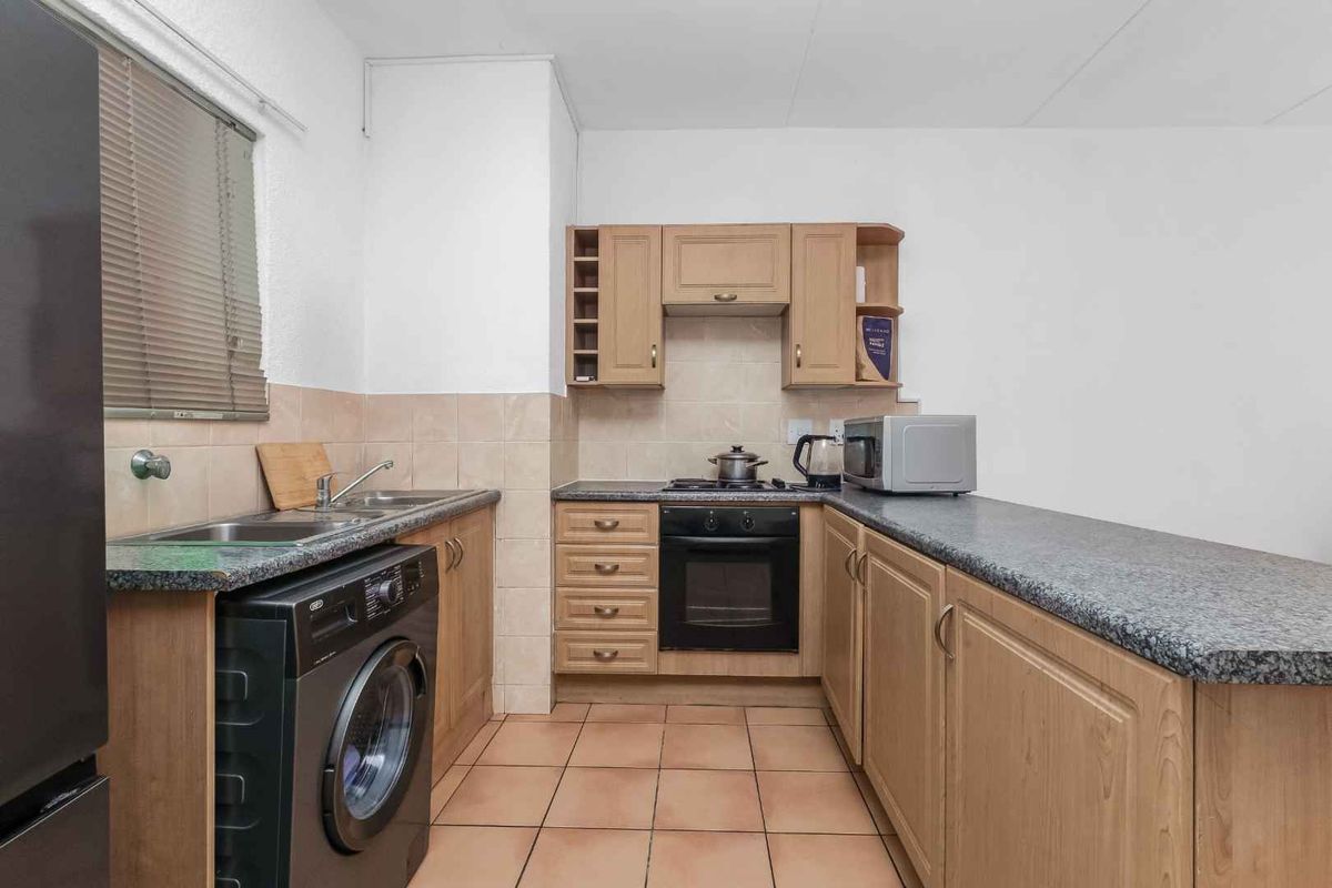 Functional kitchen featuring wood-finish cabinetry, granite-look laminate countertops, built-in oven and hob, tiled backsplash, and integrated laundry plumbing.