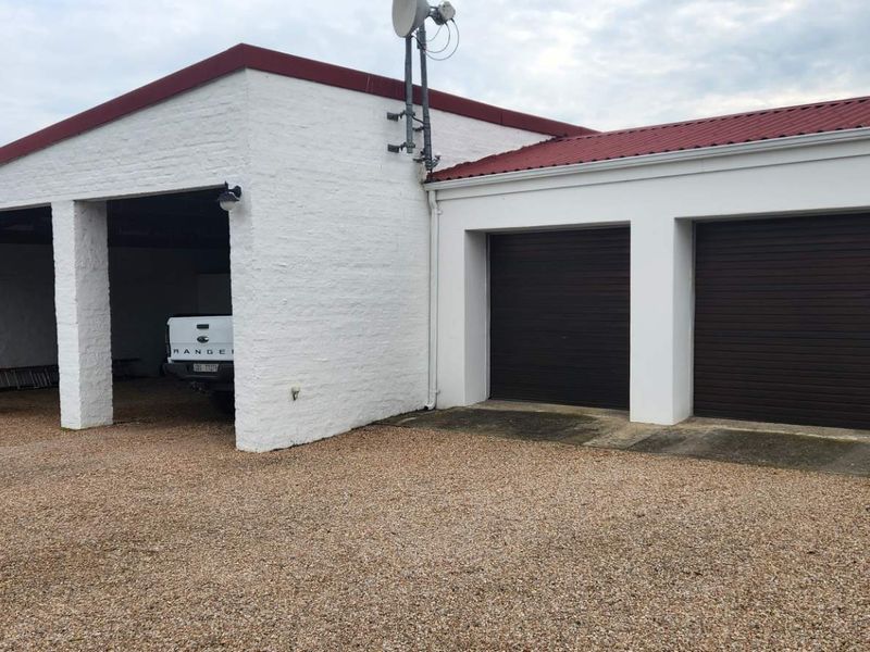 A functional farm garage facility featuring a combination of enclosed garage bays and an open-bay carport area with a gravel driveway.
