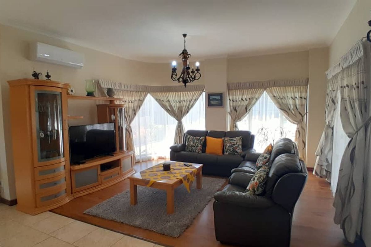 Spacious living room featuring a combination of tiled and laminate flooring, a split-system air conditioner, and decorative wall lighting.