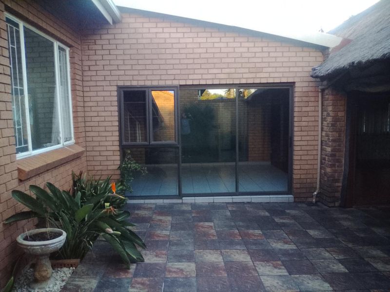 A rear exterior view featuring a brick facade, tiled patio area, and sliding glass doors leading into the home.