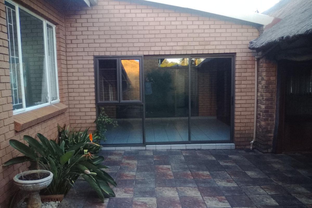 A rear exterior view featuring a brick facade, tiled patio area, and sliding glass doors leading into the home.
