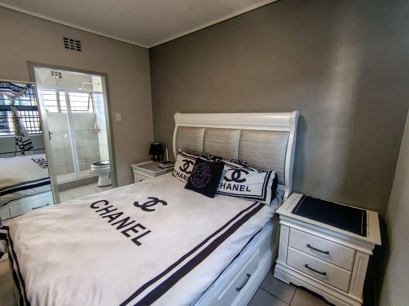 A well-maintained bedroom featuring tiled flooring and an adjoining en-suite bathroom with a glass-enclosed shower.
