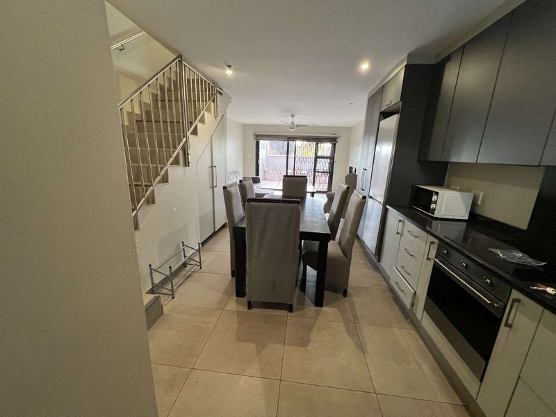 Open plan living and dining area featuring a modern kitchen with built-in cabinetry, tiled floors, and a staircase leading to the upper level.
