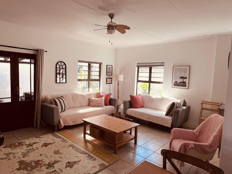 A bright and comfortable living room featuring tiled flooring, a ceiling fan, and natural light through steel-framed windows and glass-paneled french doors.