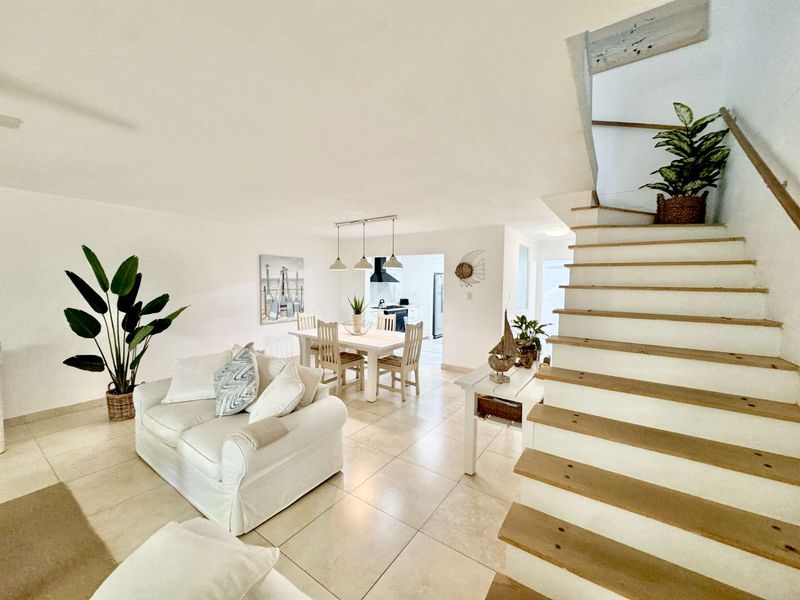 Bright open-plan living and dining area featuring tiled floors and a staircase leading to the upper level, with a view into the kitchen.