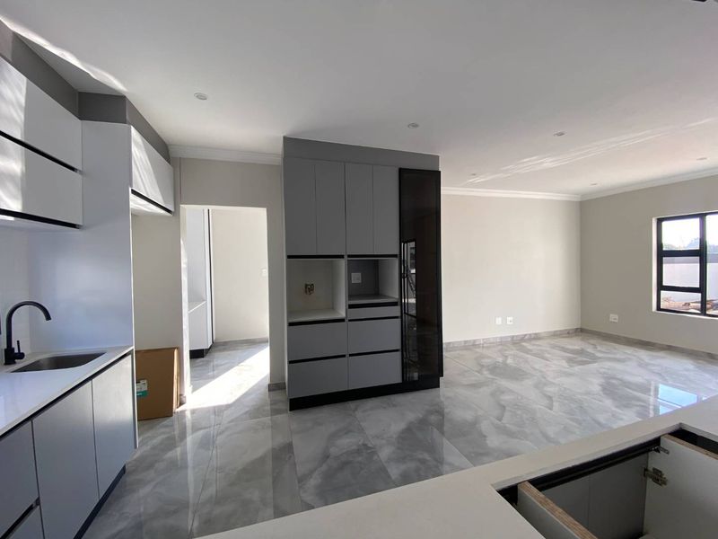 Modern open-plan kitchen and living area featuring sleek grey and white cabinetry, stone countertops, and polished porcelain floor tiles in a newly finished space.