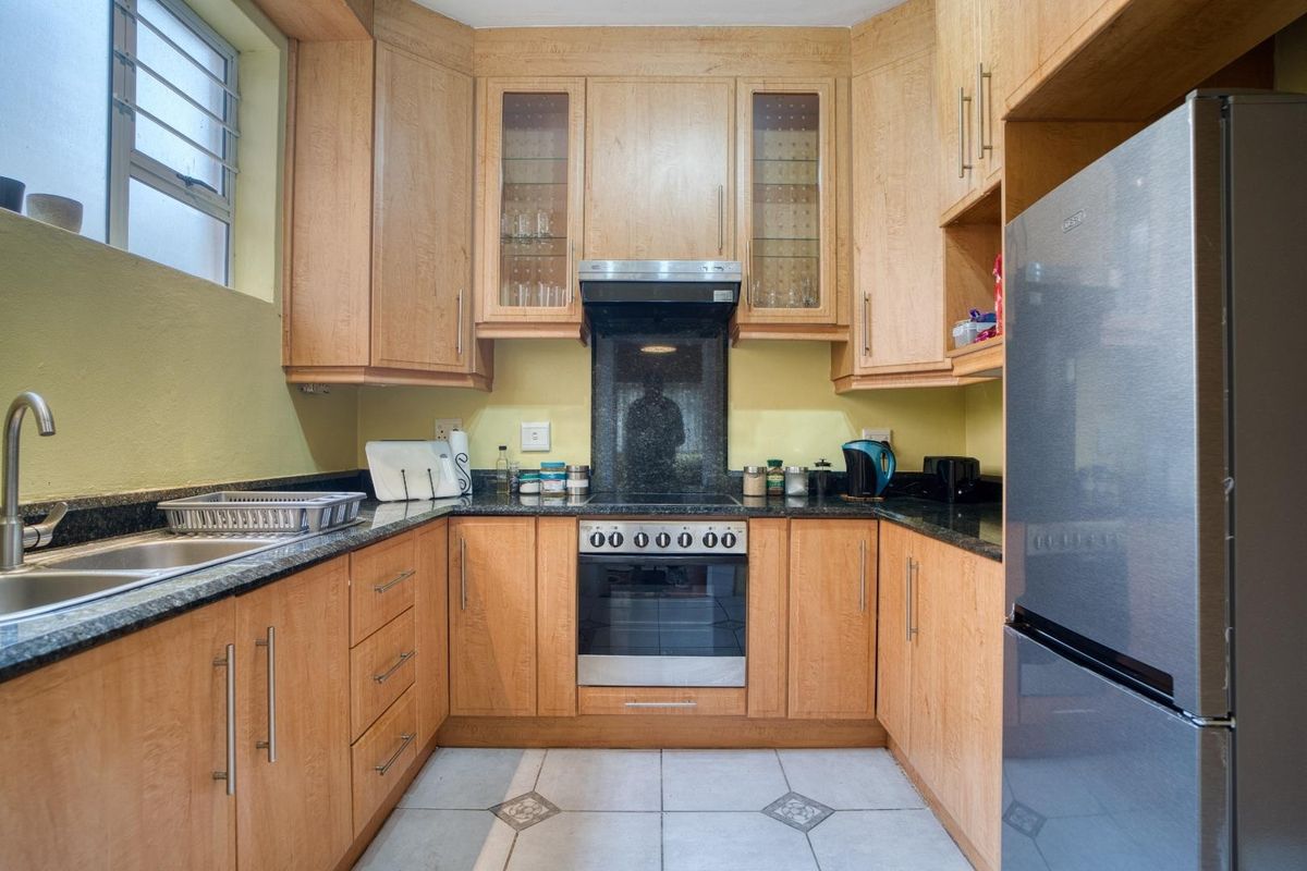 A functional kitchen featuring light wood cabinetry, dark granite countertops, a built-in oven with extractor fan, and tiled flooring.