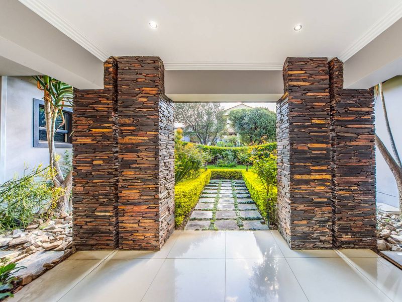 A covered patio area featuring striking stacked stone pillars, polished floor tiles, and direct access to a landscaped garden with a paved walkway.