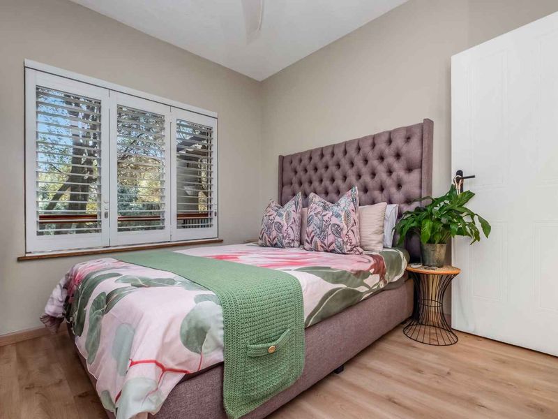 A well-maintained bedroom featuring light laminate flooring, plantation shutters, and a ceiling fan, offering a bright and comfortable living space.