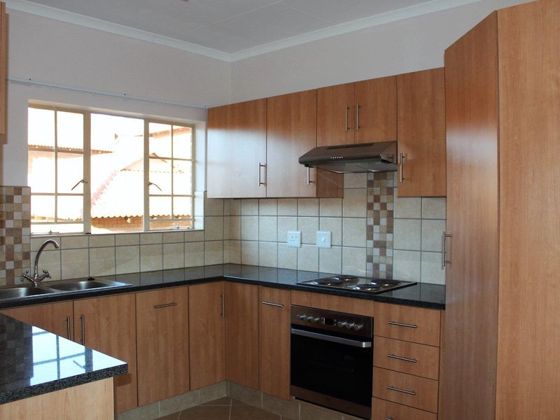 A functional kitchen featuring wood-finish cabinetry, granite countertops, a built-in oven, electric hob, and a tiled backsplash with a window for natural light.