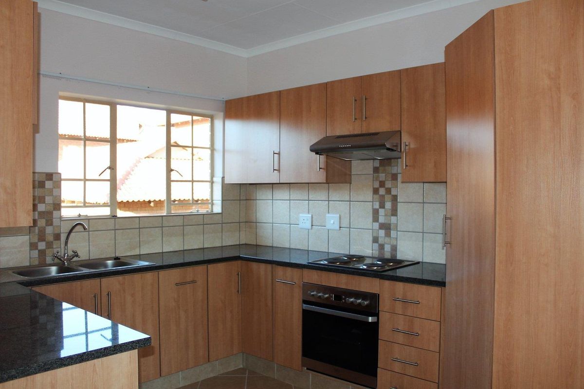 A functional kitchen featuring wood-finish cabinetry, granite countertops, a built-in oven, electric hob, and a tiled backsplash with a window for natural light.