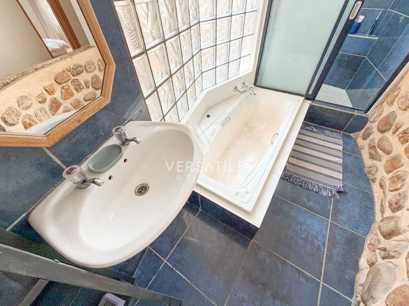 Bathroom featuring a built-in bathtub, pedestal basin, shower enclosure, and unique stone-clad walls with a glass block window for natural light.