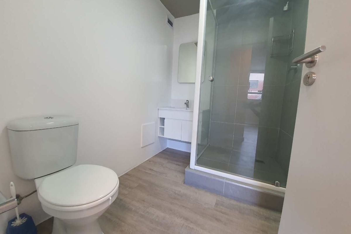A clean, modern bathroom featuring a glass-enclosed shower, a white vanity with a washbasin, and light-toned laminate flooring.