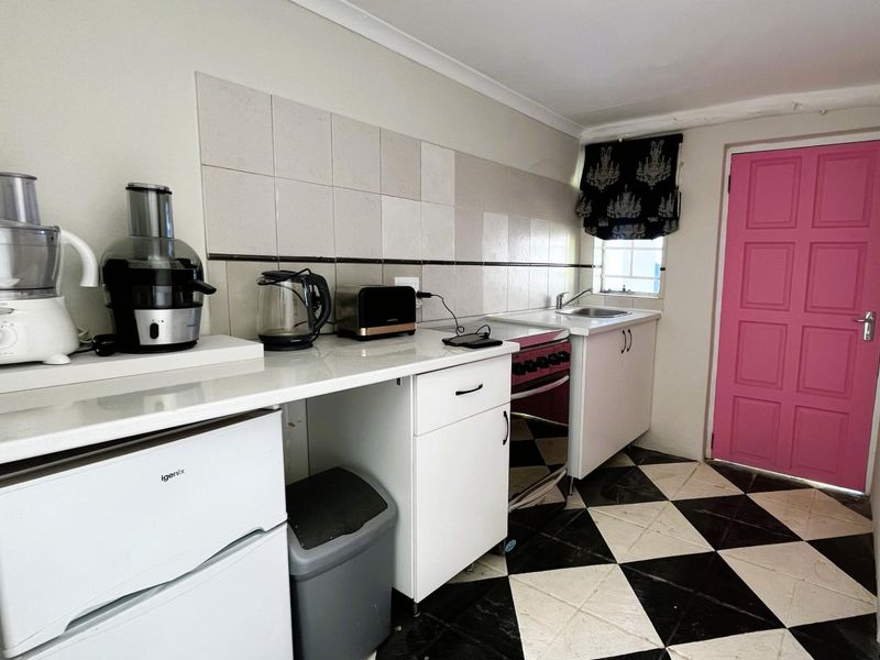 A compact kitchen featuring white cabinetry, a tiled backsplash, a freestanding oven, and a distinctive black and white checkered floor.