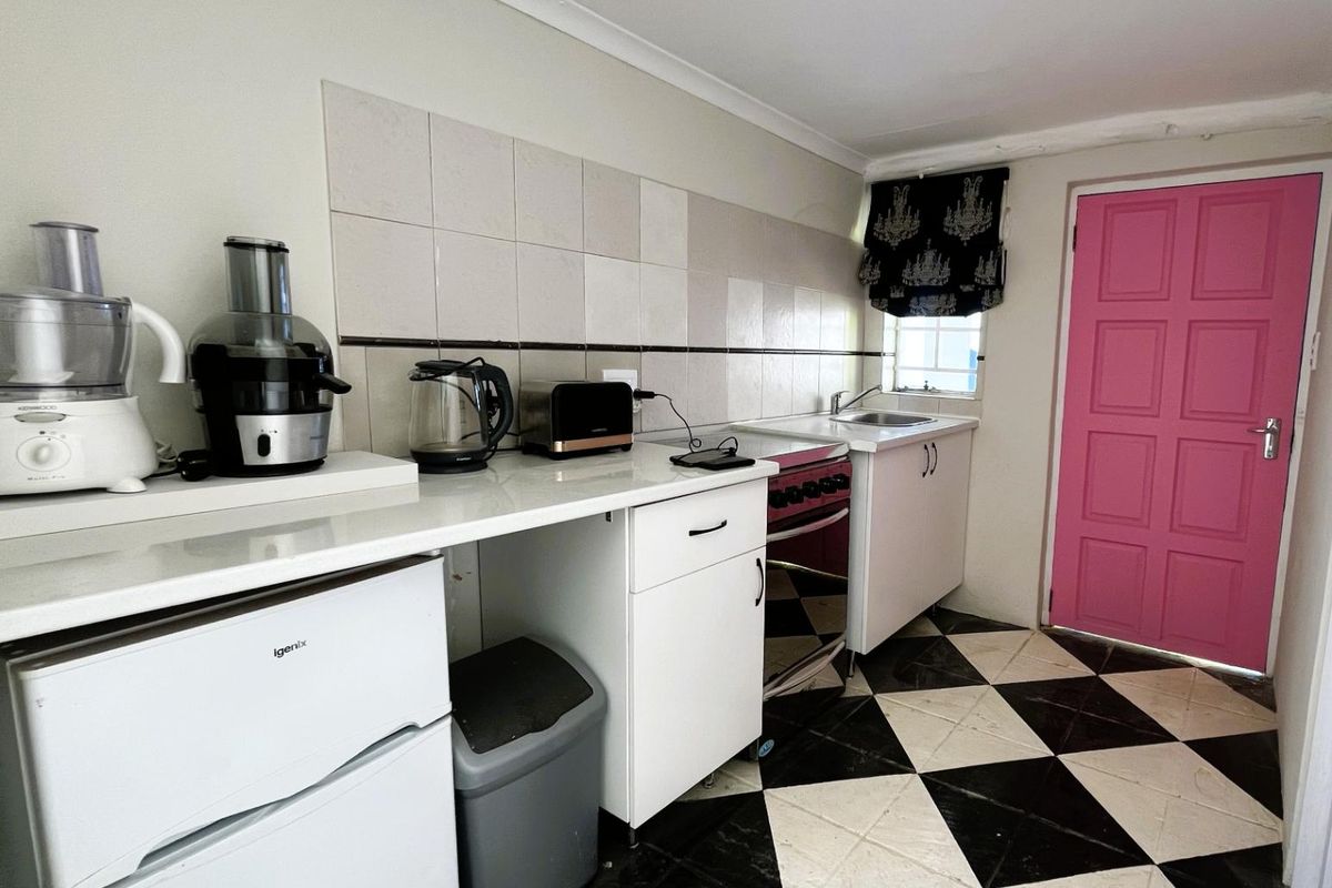 A compact kitchen featuring white cabinetry, a tiled backsplash, a freestanding oven, and a distinctive black and white checkered floor.