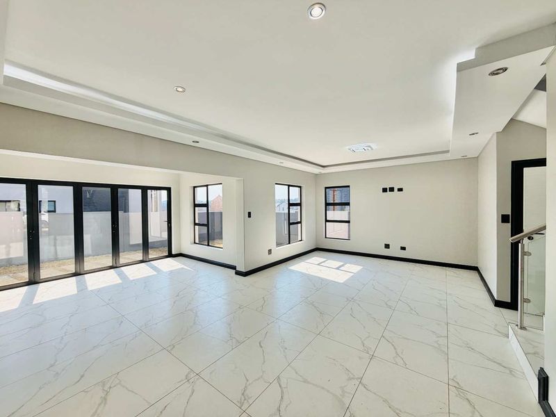 Spacious, modern open-plan living area featuring large marble-look floor tiles, recessed ceiling lighting, and black aluminium stacker doors leading to the exterior.
