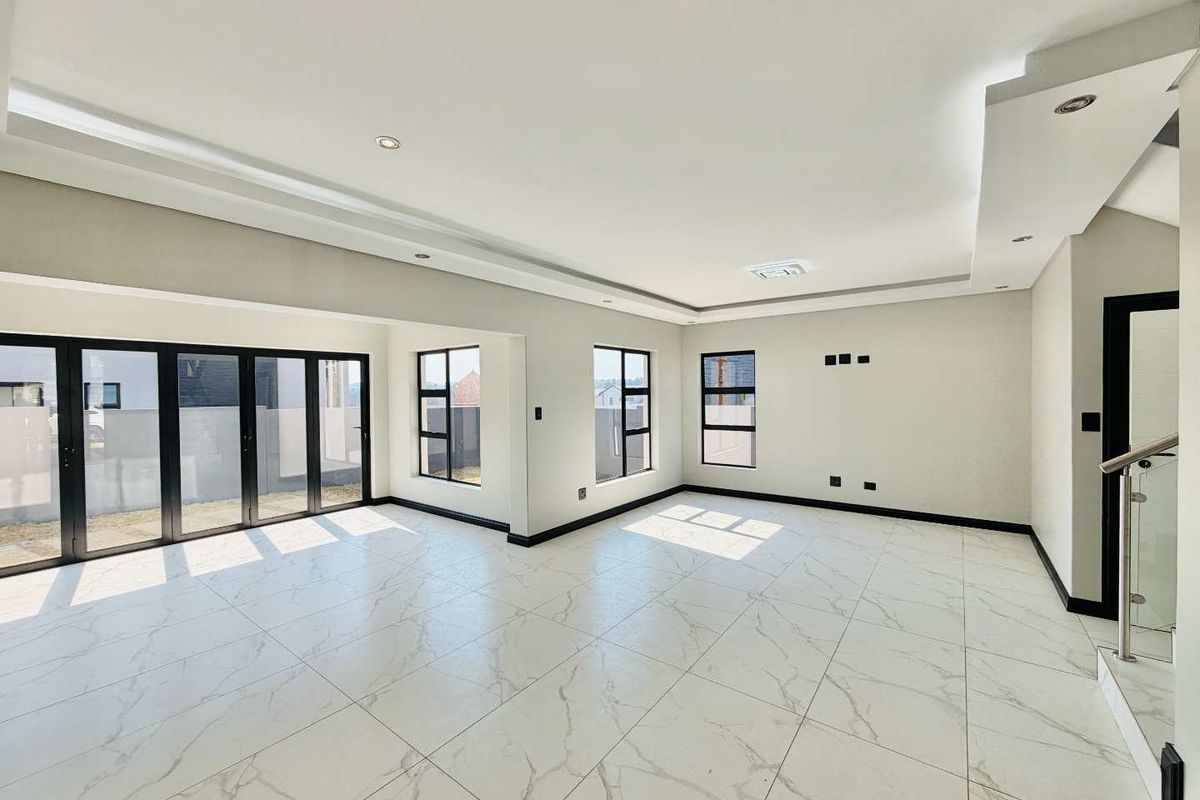 Spacious, modern open-plan living area featuring large marble-look floor tiles, recessed ceiling lighting, and black aluminium stacker doors leading to the exterior.
