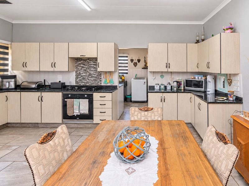 Open-plan kitchen and dining area featuring light wood-finish cabinetry, granite countertops, a gas hob, and tiled flooring, with an adjacent scullery area.