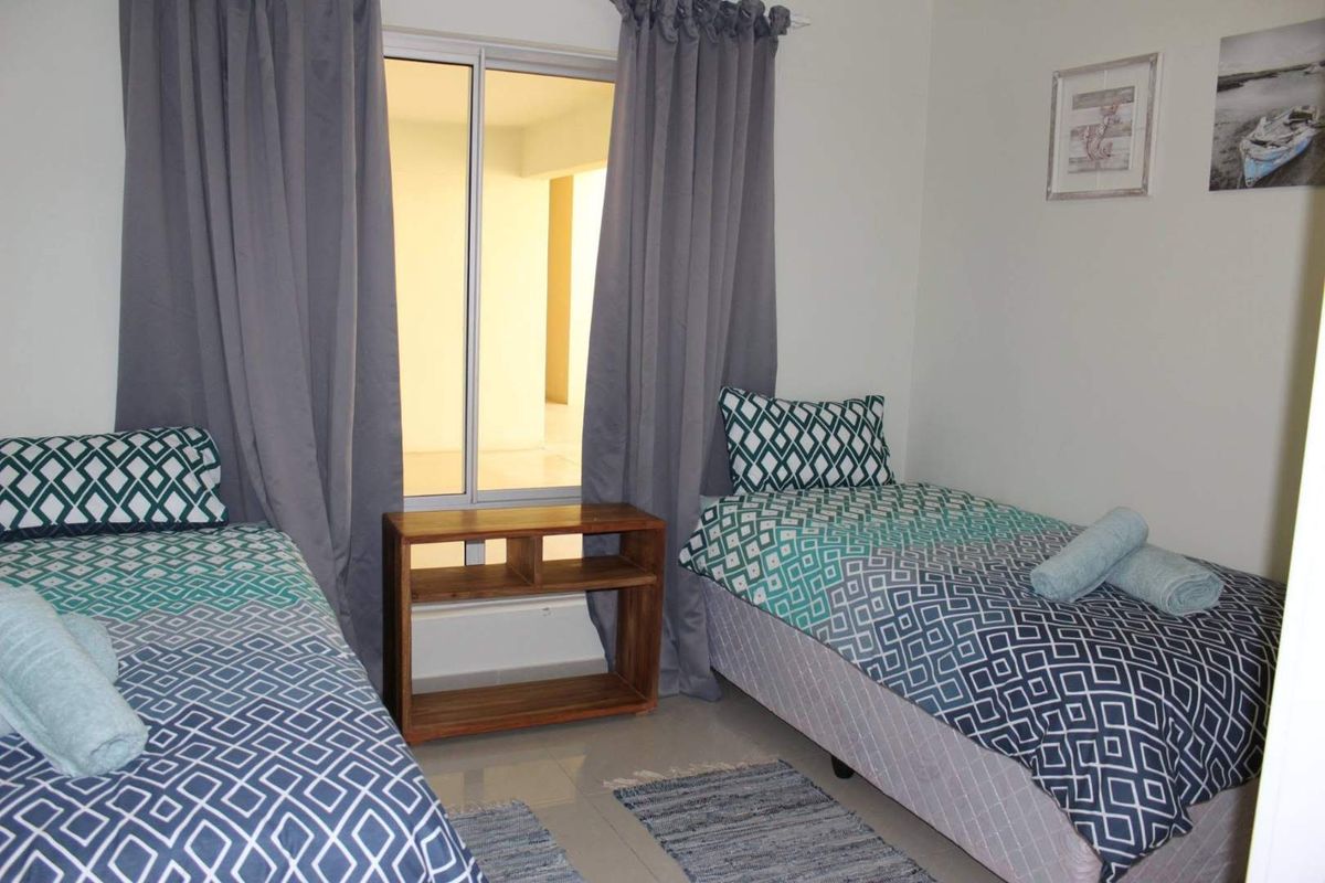 A bedroom featuring tiled flooring and a sliding window with curtains, providing natural light and access to an adjacent space.