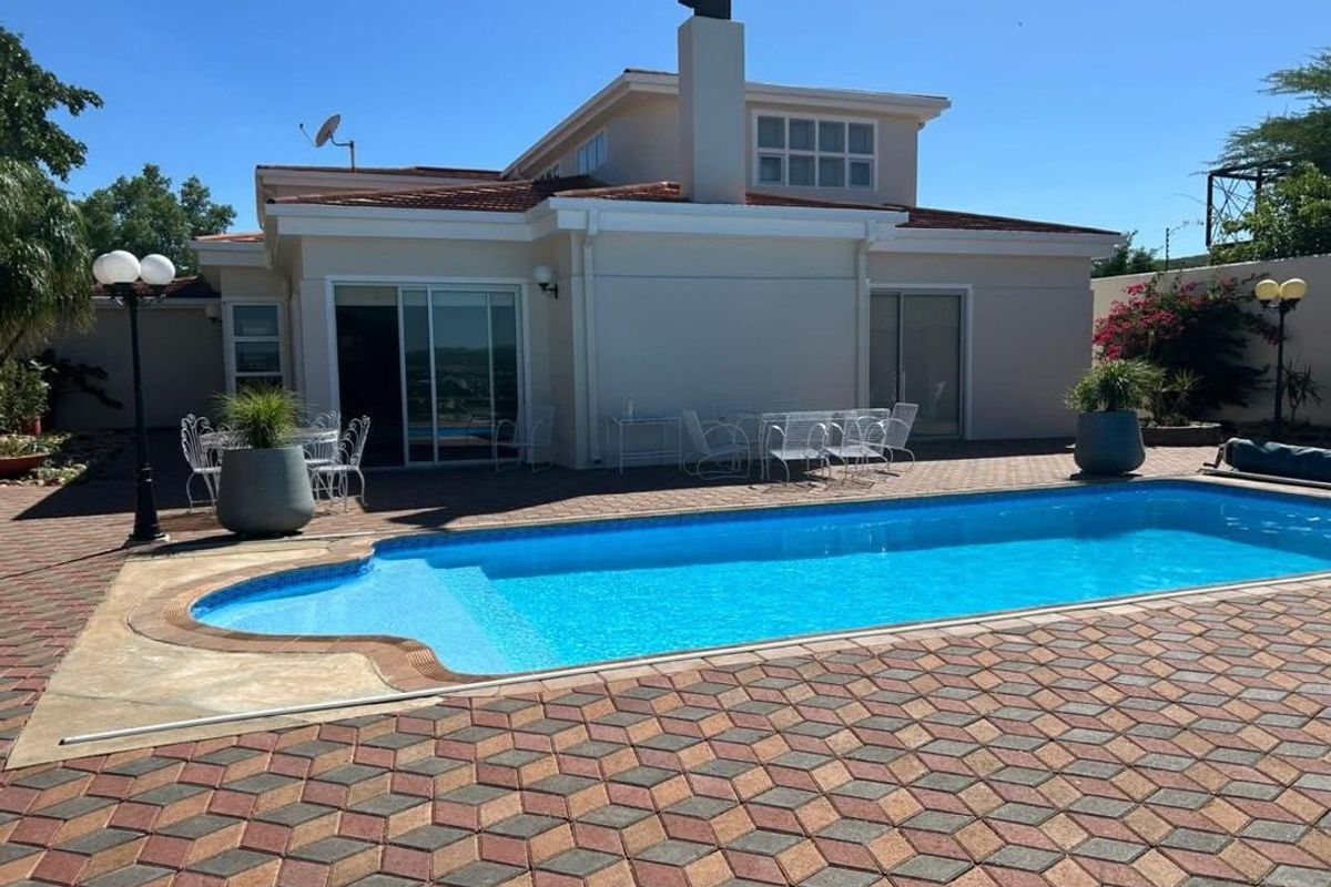 Rear view of the house featuring a swimming pool, paved patio area, and sliding glass doors leading into the living space.