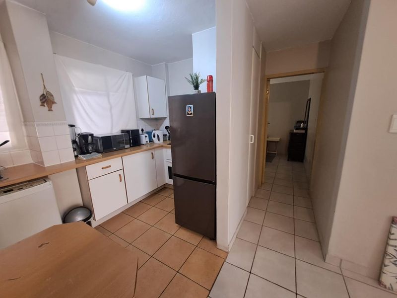 A functional kitchen featuring white cabinetry, tiled flooring, and a tiled backsplash, leading into a hallway area.