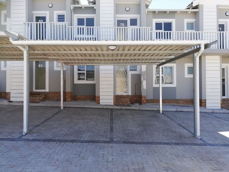 Front view of an apartment complex featuring a covered carport, paved driveway, and private balconies with modern grey and white facade finishes.